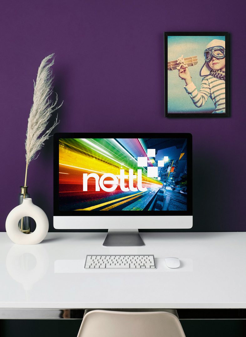 iMac with Nettl logo on a white desk against a purple wall, with framed artwork. Nettl of Chesterfield – web, print & design experts